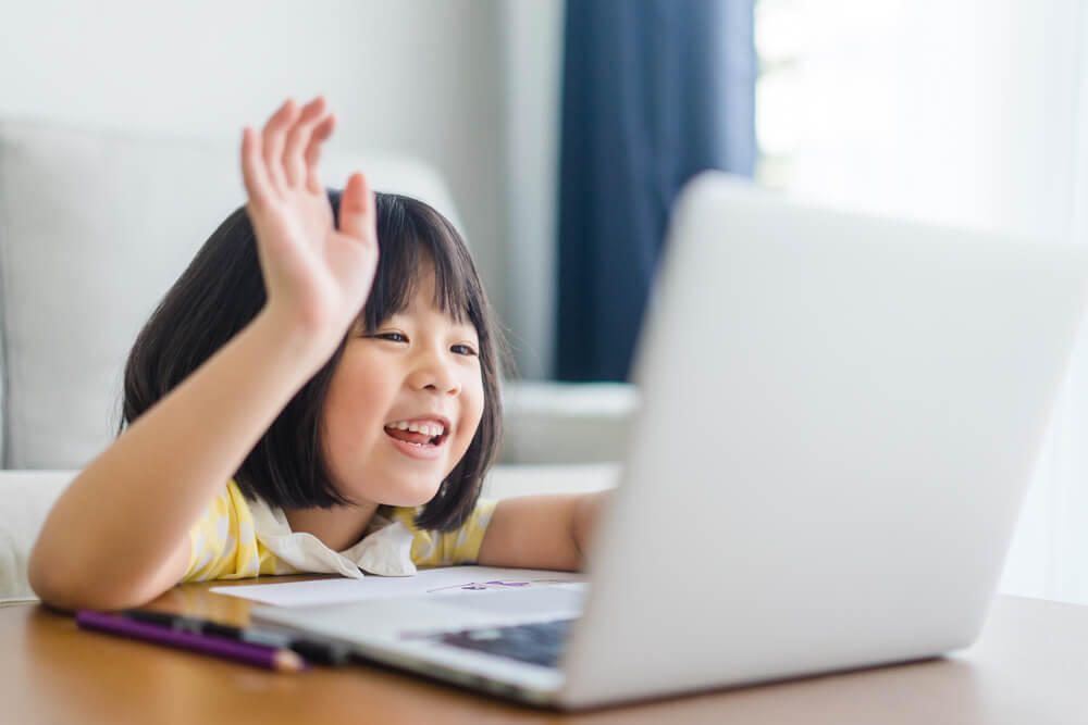 little girl waving to white laptop - teaching children with autism online
