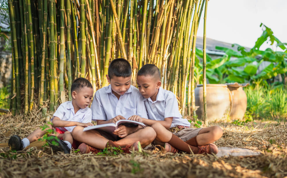 teaching with technology - three boys reading a book at the garden